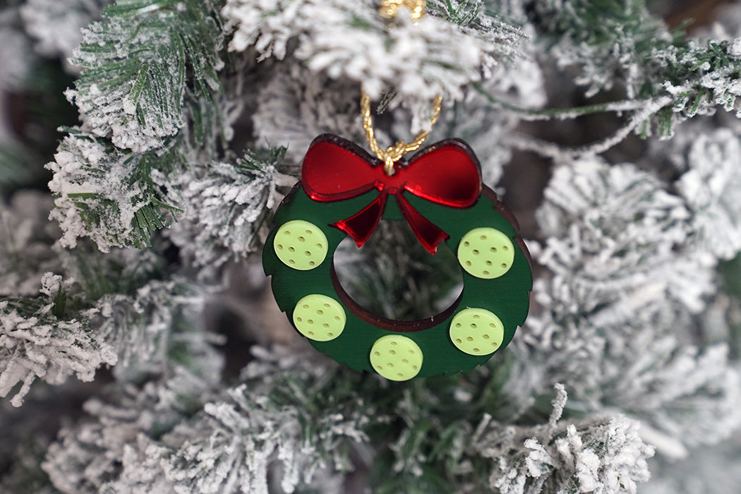 Christmas pickleball ornament shaped like a wreath with a red bow on a snow-covered tree.